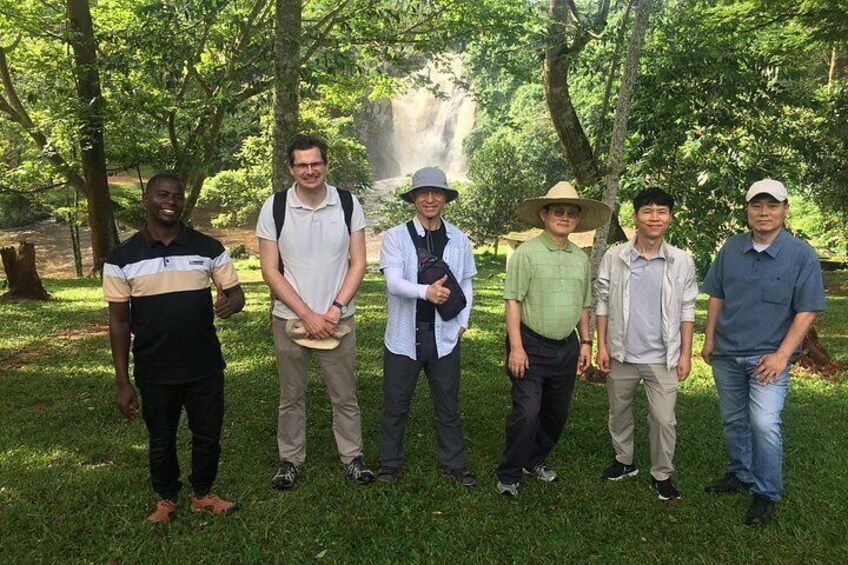 A group of people standing in a park with trees and a waterfall in the background. 4