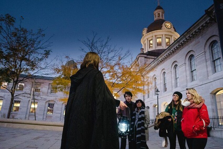 A person in a long black coat walking with a group of people in an urban setting with a historic building in the background. 2
