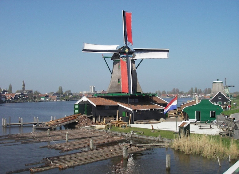 A traditional windmill by a water body, surrounded by houses and a clear sky. 1