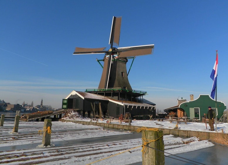 A windmill with a flag, a frozen river, and buildings in the background. 5
