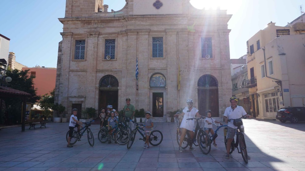 A group of cyclists in front of a historic building with arched windows and a central door. 5