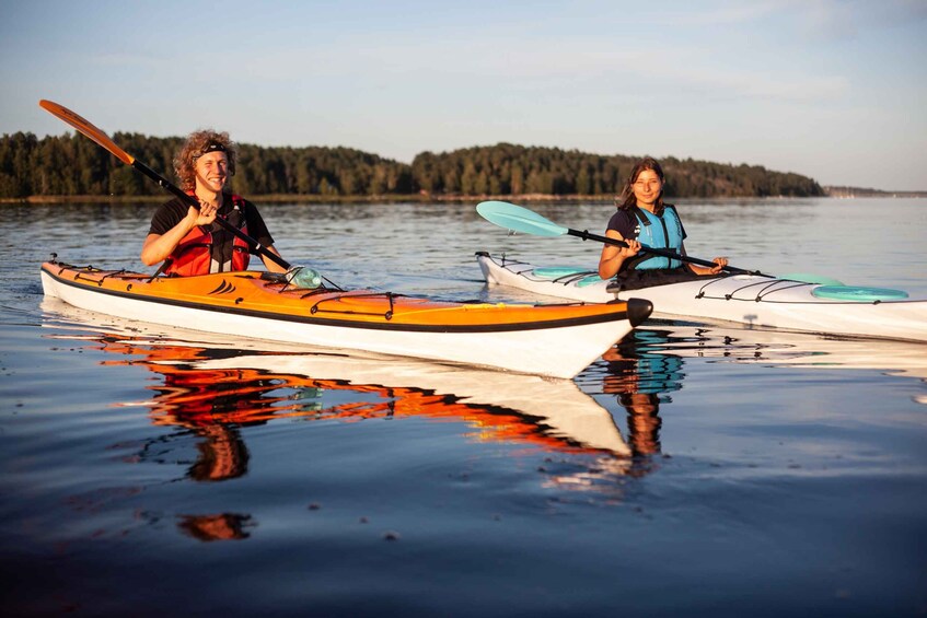 Due persone che fanno kayak su un lago tranquillo, con i riflessi delle canoe e degli alberi nell'acqua. 1