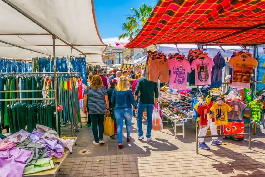 A bustling outdoor market with various stalls selling clothing and accessories. 3