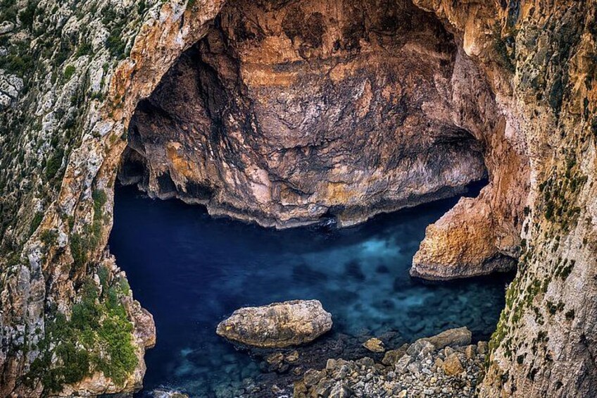 A rocky coastal landscape with a deep blue sea, a narrow passageway, and a rugged cliff. 5
