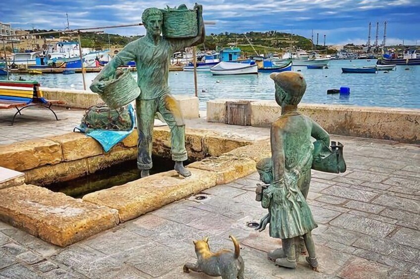 A statue of a man carrying a basket and a child holding a bucket by a waterfront. 5