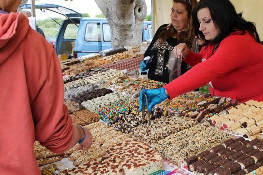 A person in a red hoodie and blue gloves handling a tray of assorted baked goods at a market. 2