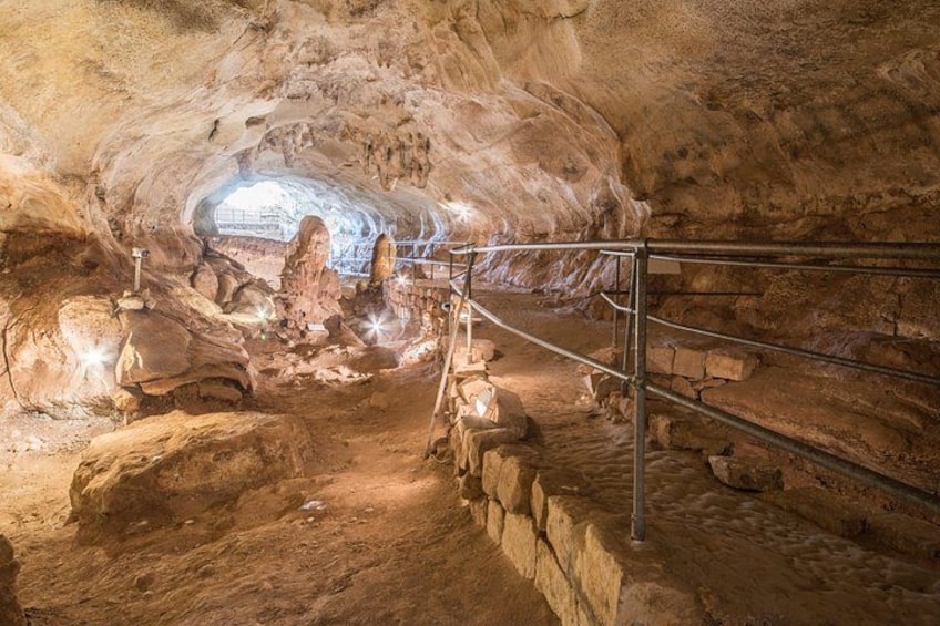 A cave interior with a central rock formation, metal railings, and a light source. 3