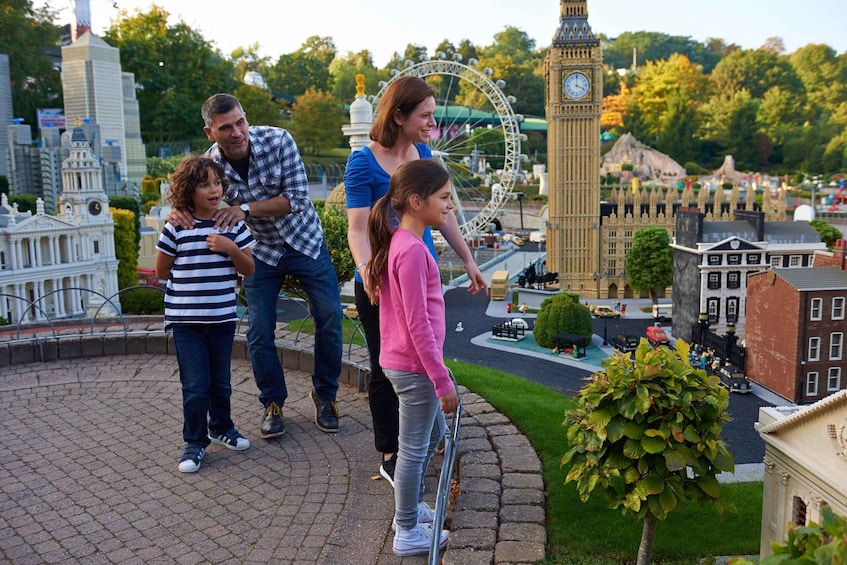 A family standing on a paved area with a miniature model of London, including the Big Ben clock tower and a Ferris wheel. 5