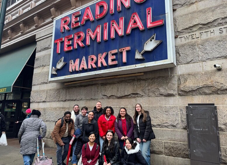 A group of people in front of a sign that reads 'READING TERMINAL MARKET' on a stone building. 3
