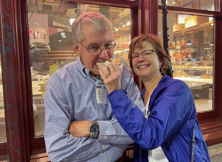 Two people standing in front of a window with a food display inside. 2