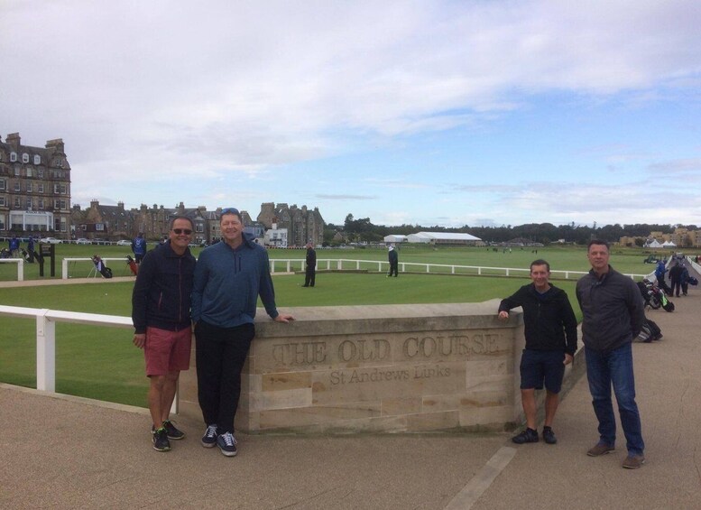 A group of people standing in front of a sign that reads "THE OLD COURSE" with a golf course in the background. 1