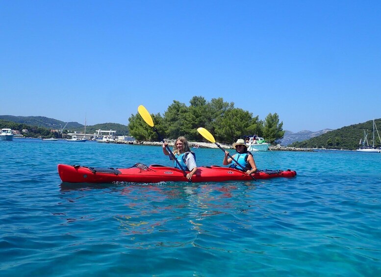 Dos personas kayakendo en un lago azul y tranquilo, con barcos y una colina boscosa al fondo. 5