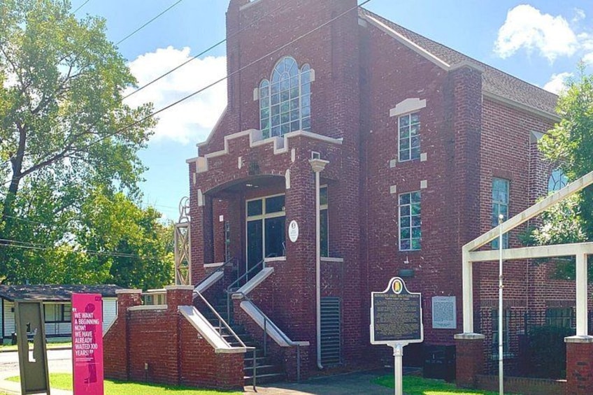 A brick building with a large arched entrance, a staircase leading up to the entrance, and a signboard. 3