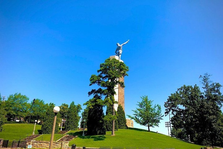 A statue on a tall column in a park with a clear blue sky. 2