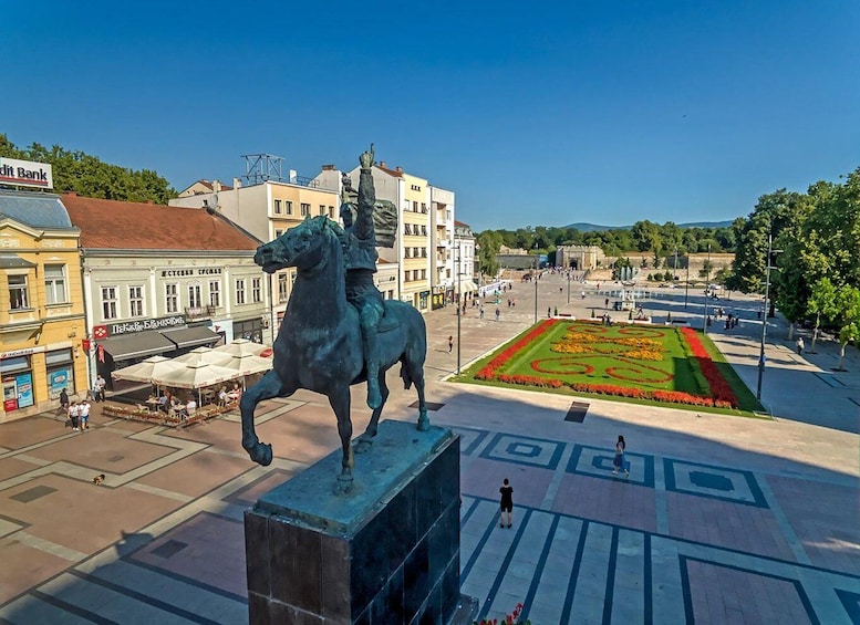 A statue of a man on a horse in a public square with buildings and a patterned garden in the background. 5
