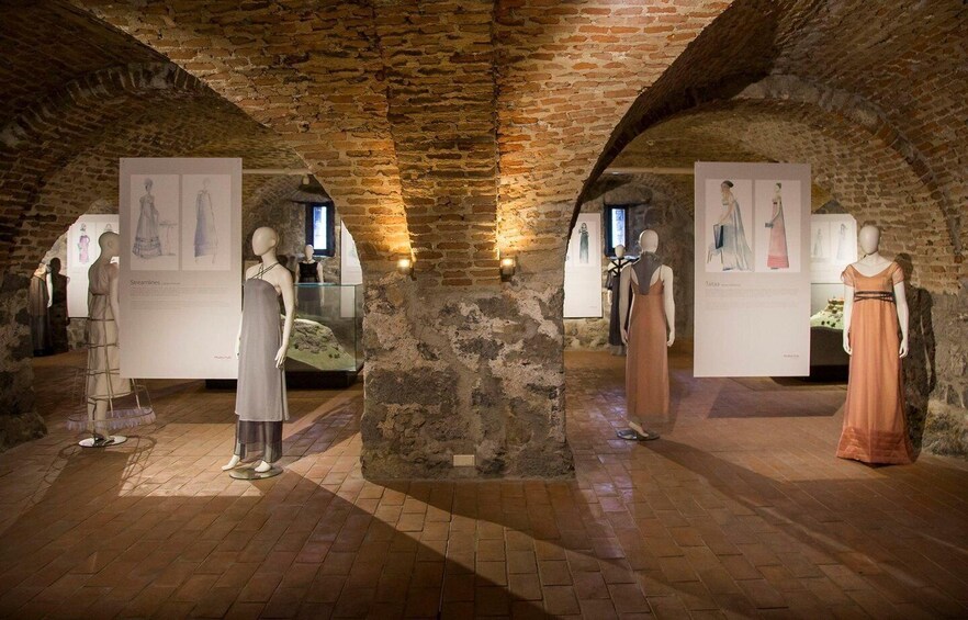 A museum with mannequins in dresses, brick walls, and stone flooring. 3