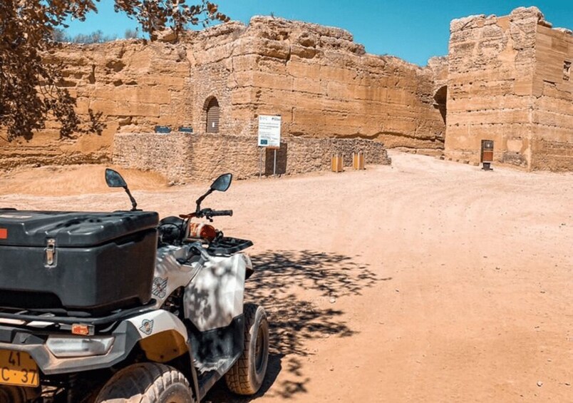A quad bike parked in front of ancient ruins with a clear sky. 2