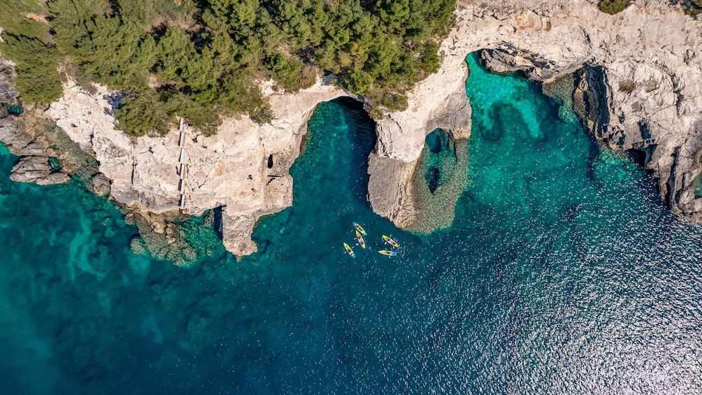 A coastal landscape with clear turquoise waters, rocky cliffs, and a forested area. 4