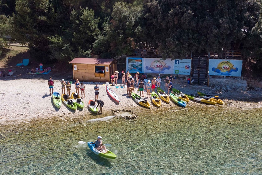 A group of people on a beach with kayaks lined up and a small wooden structure. 2