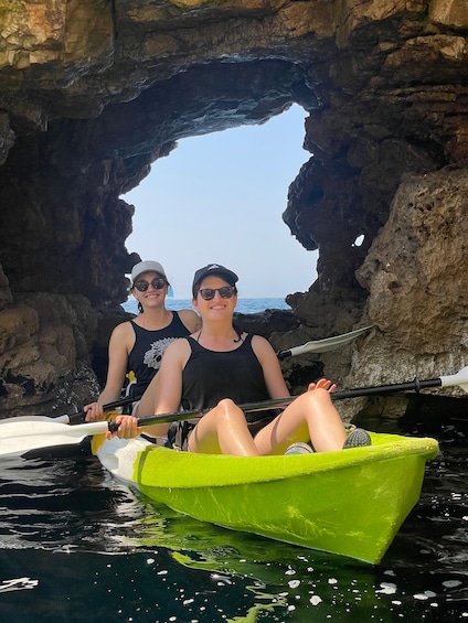 Two people kayaking in a green kayak through a rocky arch formation. 5