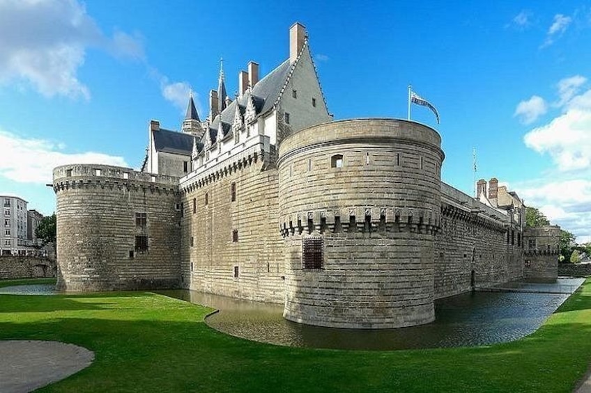 Un castello storico in pietra con un fossato, circondato da prati curati e un cielo azzurro terso. 1