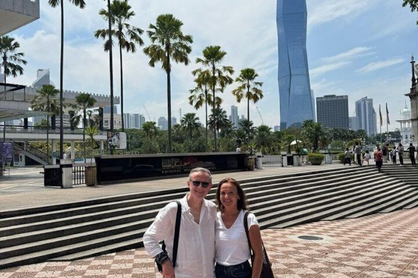 A couple posing in front of a modern skyscraper with palm trees and a patterned pavement. 4