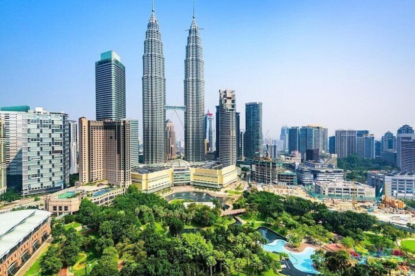 A cityscape with prominent skyscrapers, lush greenery, and a clear blue sky. 1
