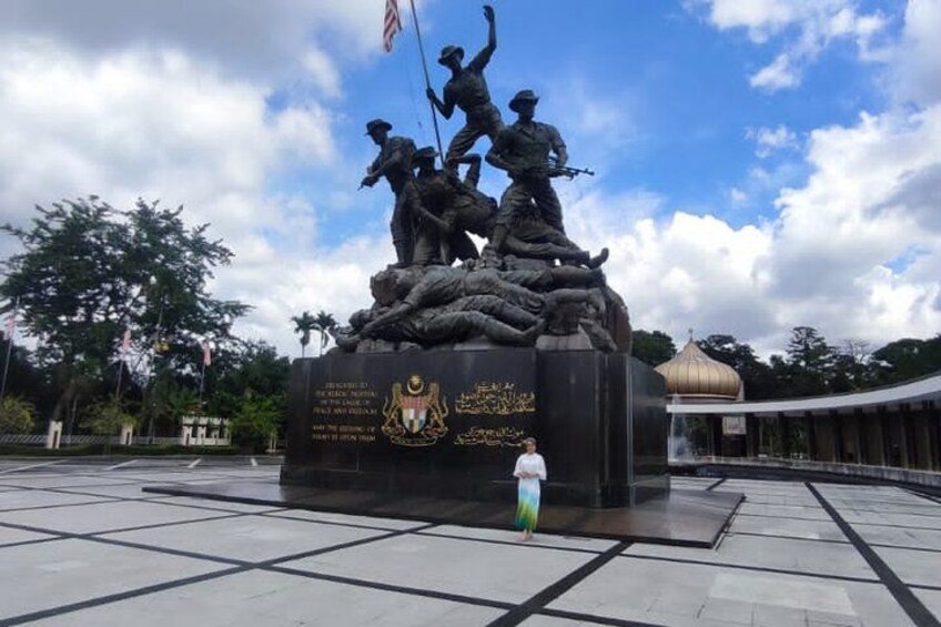 Une statue de soldats, placée sur un piédestal et surmontée d’un drapeau, est entourée d’une place dallée et d’un bâtiment coiffé d’un dôme. 4