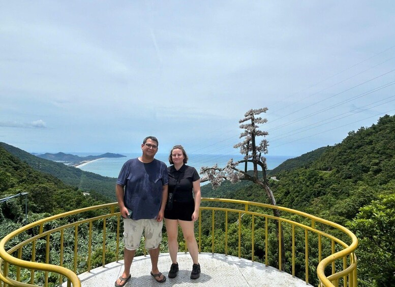 A couple standing on a viewing platform with a coastal landscape in the background. 2