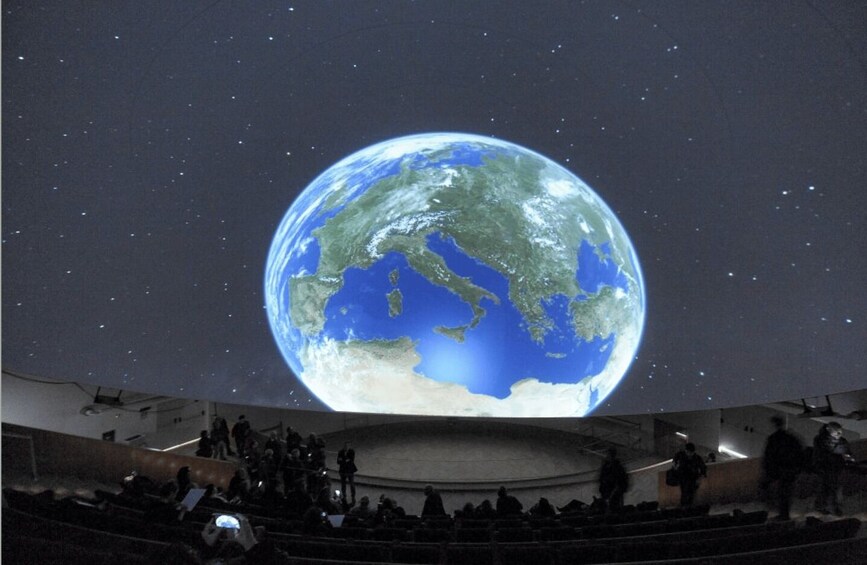 A planetarium with a large projection of Earth, audience seating, and a stage. 2