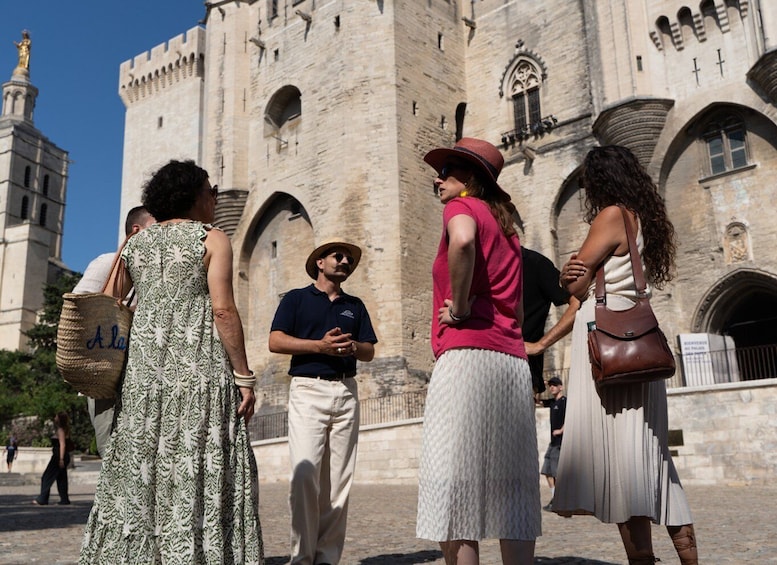 Un groupe de personnes se tient devant un bâtiment historique en pierre, doté d’arcades et d’une tour. 1