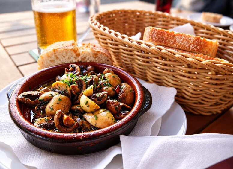 Un bol de ragoût aux champignons et aux pommes de terre, un verre de bière et un panier de pain sur une table en bois. 1