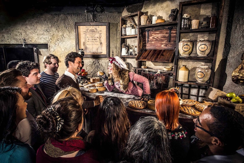 A group of people in a rustic kitchen with wooden shelves, jars labeled 'Yeast' and 'Yeast', and a sign reading 'Best Flour'. 1