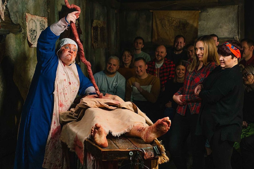 A person in blue holding a rope, standing over a table with a person lying on it, surrounded by a group of people. 5