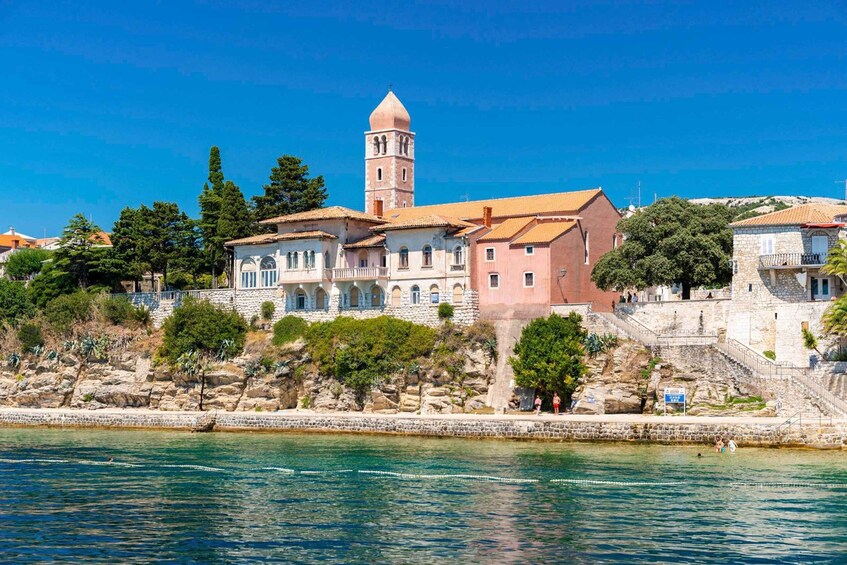 A coastal town with a prominent tower, stone buildings, and a clear blue sky. 5