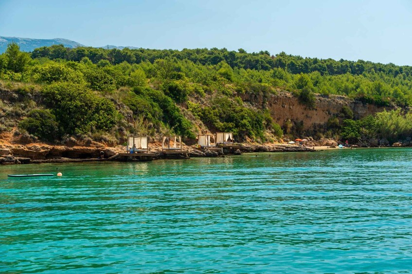 A coastal area with clear turquoise waters, a rocky shoreline, and a forested hill in the background. 2