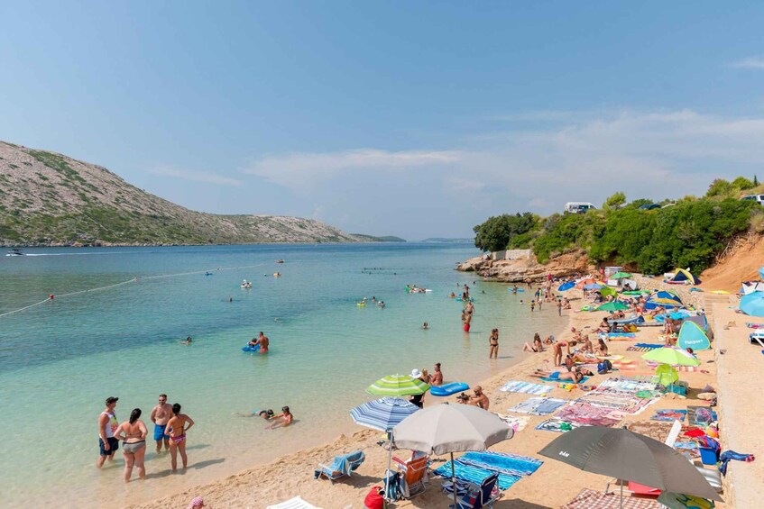 A crowded beach with people swimming and sunbathing, umbrellas, and beach chairs. 2