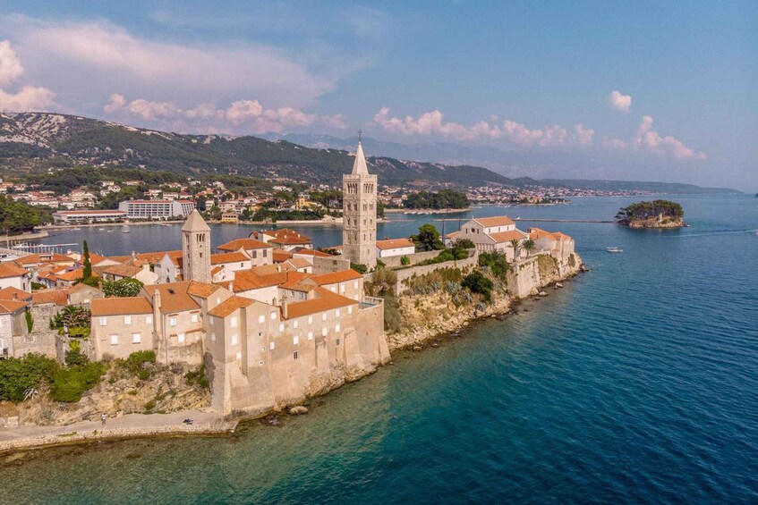 A coastal town with historic buildings, a prominent tower, and a clear view of the surrounding water and hills. 3