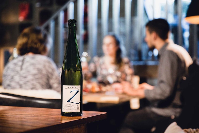 Une bouteille de vin d’Alsace, de la marque Z, posée sur le comptoir d’un bar, avec des personnes en arrière-plan. 3
