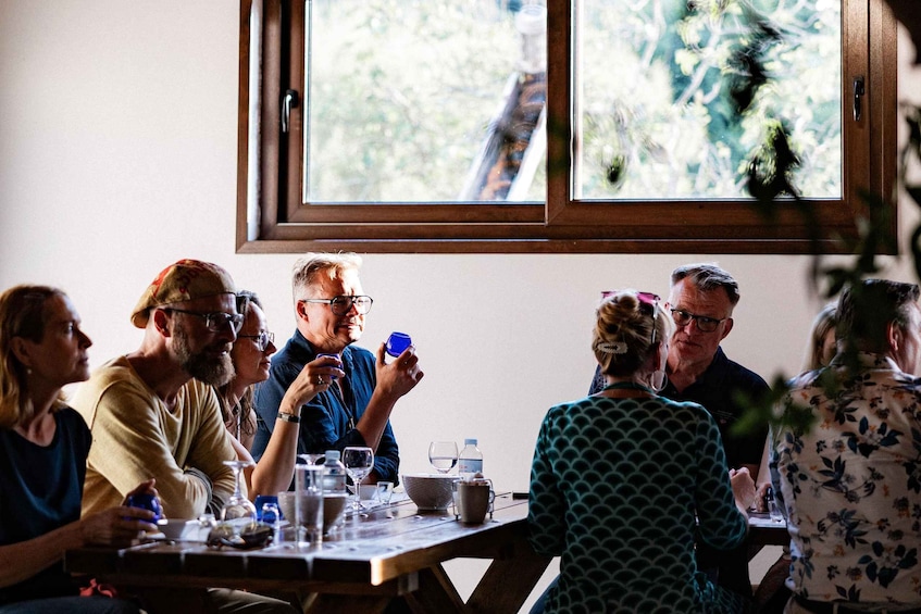 A group of people sitting around a wooden table at a restaurant with a view of trees outside. 2