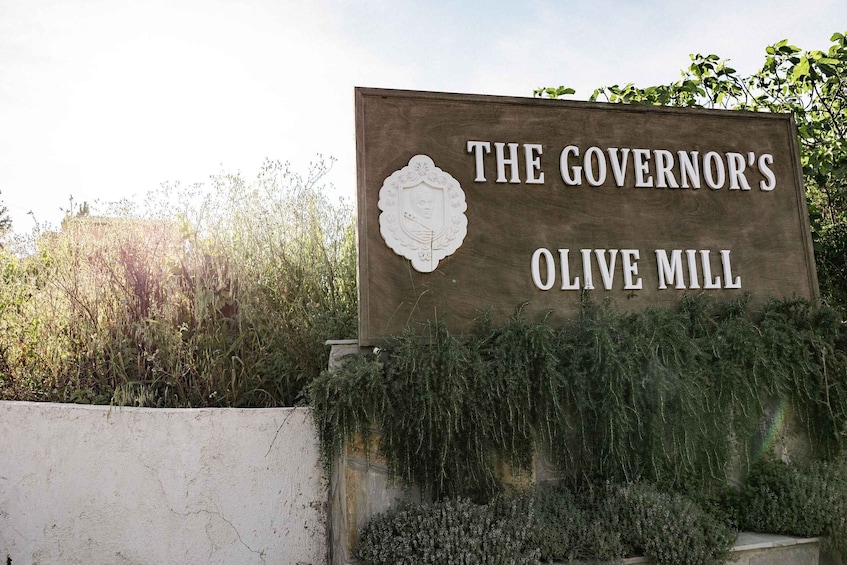 A sign reading "The Governor's Olive Mill" with a decorative emblem. 1
