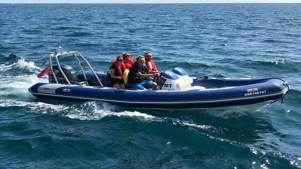 A blue inflatable boat with three people wearing life jackets on the water. 3
