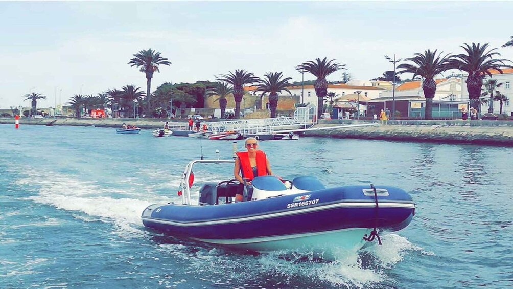A person riding a blue motorboat on a calm waterway, with palm trees and buildings in the background. 1