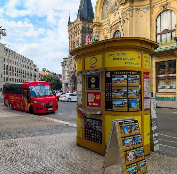 A yellow tourist information kiosk with signs for city tours, river cruises, and excursions. A red bus is parked nearby. 2