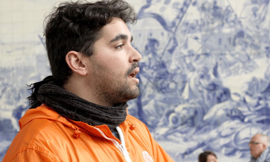 A person in an orange jacket with a black scarf, standing in front of a blue and white mural. 2