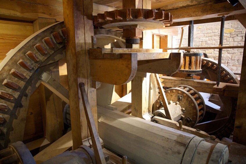 A large wooden water wheel with gears and a stone wall in the background. 5