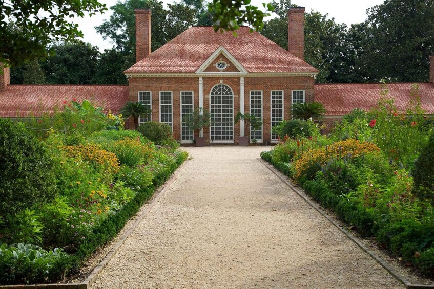 A brick building with a central entrance, surrounded by a gravel path and lush gardens. 4
