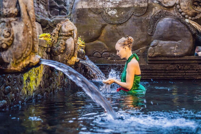 Una persona con un abito verde in piedi in una vasca d'acqua con una scultura in pietra e un ruscello. 2