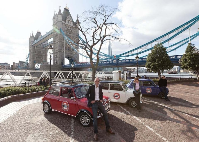 A red vintage car with a white license plate parked in front of the Tower Bridge. 2