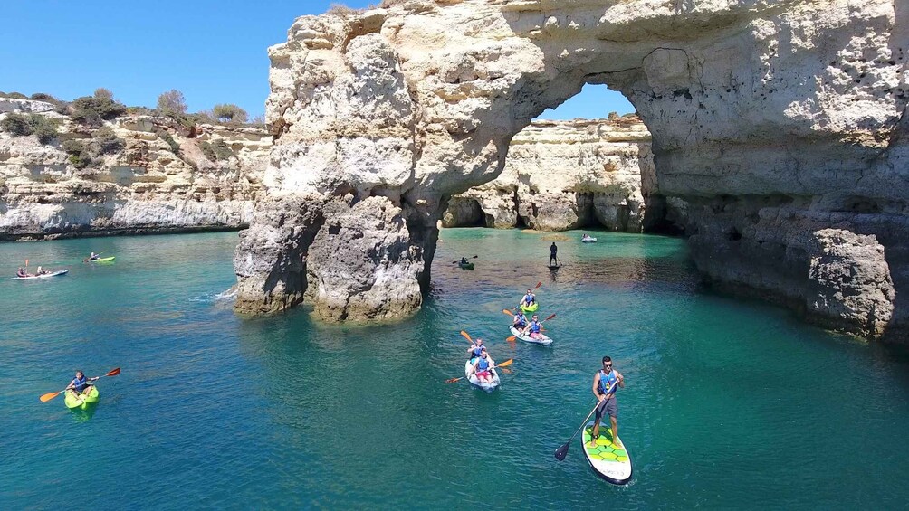 Kayakers and paddleboarders in a coastal area with a large rock arch. 1